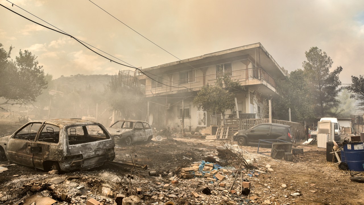 This photograph taken on August 23, 2023 shows burnt cars near a house as a wildfire spreads in Acharnes, north of Athens. Greek firefighters on August 23, 2023 struggled to contain uncontrolled fires throughout the country for a fifth day, several of them bordering an acrid, smoke-filled Athens. (Photo by Spyros BAKALIS / AFP) / The erroneous mention[s] appearing in the metadata of this photo by Spyros BAKALIS has been modified in AFP systems in the following manner: [Acharnes] instead of [Archanes]. Please immediately remove the erroneous mention[s] from all your online services and delete it (them) from your servers. If you have been authorized by AFP to distribute it (them) to third parties, please ensure that the same actions are carried out by them. Failure to promptly comply with these instructions will entail liability on your part for any continued or post notification usage. Therefore we thank you very much for all your attention and prompt action. We are sorry for the inconvenience this notification may cause and remain at your disposal for any further information you may require.