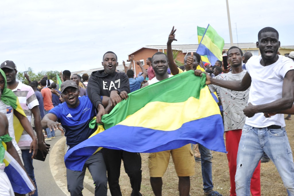 Residents gesture and hold a Gabon national flag as they celebrate in Libreville on August 30, 2023 after a group of Gabonese military officers appeared on television announcing they were "putting an end to the current regime" and scrapping official election results that had handed another term to veteran President Ali Bongo Ondimba. In a pre-dawn address, a group of officers declared "all the institutions of the republic" had been dissolved, the election results cancelled and the borders closed. (Photo by AFP)