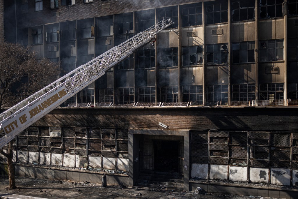 A ladder from a fire engine is pictured reaching into a burned apartment block in Johannesburg on August 31, 2023. More than 70 people have died in a fire that engulfed a five-storey building in central Johannesburg on August 31, 2023, the South African city's emergency services said. (Photo by Michele Spatari / AFP)