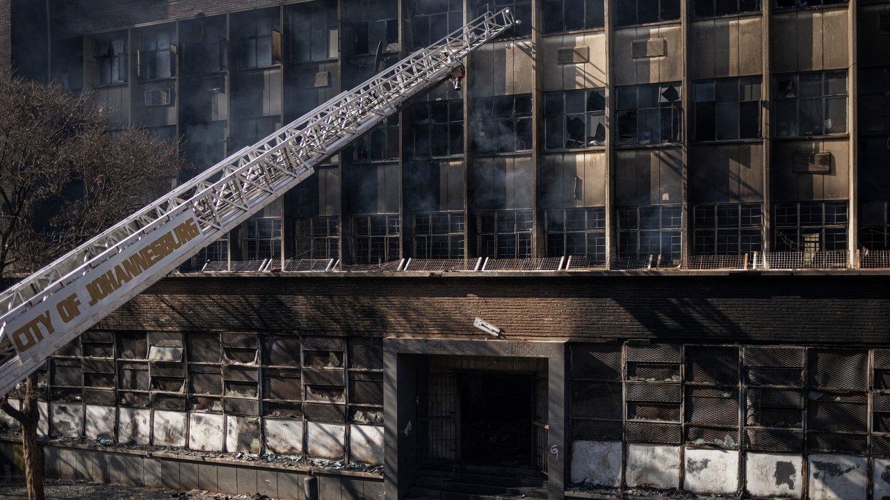A ladder from a fire engine is pictured reaching into a burned apartment block in Johannesburg on August 31, 2023. More than 70 people have died in a fire that engulfed a five-storey building in central Johannesburg on August 31, 2023, the South African city's emergency services said. (Photo by Michele Spatari / AFP)