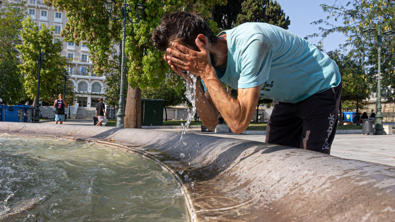 Um homem é visto espirrando água da fonte em seu rosto para se refrescar, em meio à onda de calor na Grécia. 15/07/2023