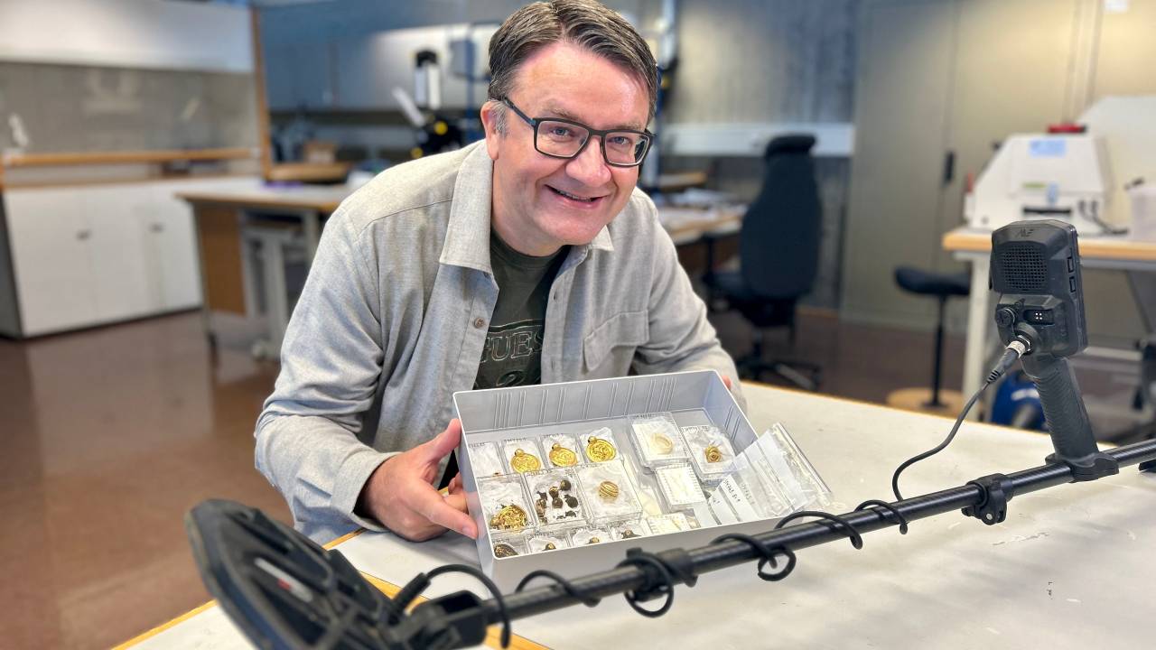 Handout photo released on September 7, 2023 by the Museum of Archaeology and the University of Stavanger (UiS), south-western Norway, shows amateur archaeologist Erlend Bore posing with a gold treasure photographed shortly after he found them in the ground with a metal detector on the island of Rennesøy in Stavanger. The treasure consists of nine gold medallions and pearls that once formed a luxurious necklace, as well as three gold rings, the University of Stavanger announced on September 7, 2023. It was discovered at the end of August on a farmer's property near Stavanger by an amateur archaeologist, Erlend Bore, who had bought a metal detector after his doctor and physiotherapist advised him to be more physically active. (Photo by Anniken Celine Berger / various sources / AFP) / Norway OUT