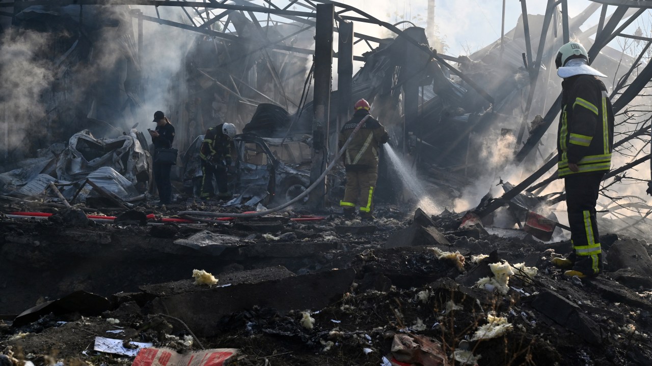 Firefighters push out a fire as police experts look for fragments of missile at a crater on an industrial area of the Ukrainian capital of Kyiv, after a massive overnight missile attack to Ukraine on September 21, 2023. Ukraine said on september 21, 2023 its air defence systems had brought down three dozen Russian cruise missiles overnight in Moscow's latest barrage that left dead and injured throughout the country. (Photo by Sergei SUPINSKY / AFP)