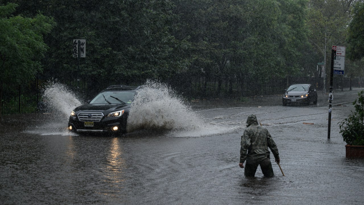 Um homem limpa um ralo enquanto um carro atravessa as enchentes no Brooklyn, em Nova York. 29/09/2023