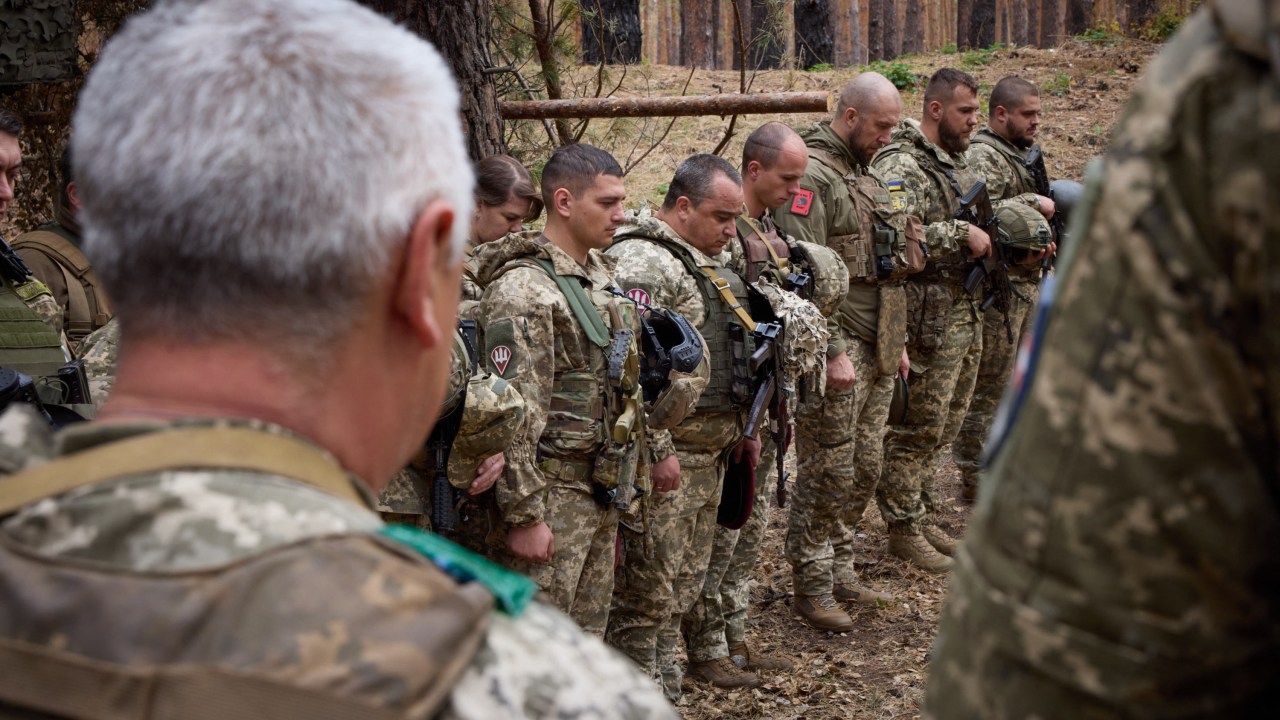 This handout photograph taken and released by the Ukrainian Presidential Press Service on October 3, 2023 shows serviceman bowing their heads in rememberance for a dead colleague during the visit of the Ukrainian President (not pictured) to the 103rd Separate Brigade of the Territorial Defense Forces of the Armed Forces of Ukraine, the 68th Separate Yeger Brigade, and the 25th Separate Sicheslav Airborne Brigade, which are performing combat missions in the Kupyansk-Lyman area, in Kharkiv region. (Photo by Handout / UKRAINIAN PRESIDENTIAL PRESS SERVICE / AFP) / RESTRICTED TO EDITORIAL USE - MANDATORY CREDIT "AFP PHOTO / UKRAINIAN PRESIDENTIAL PRESS SERVICE" - NO MARKETING NO ADVERTISING CAMPAIGNS - DISTRIBUTED AS A SERVICE TO CLIENTS