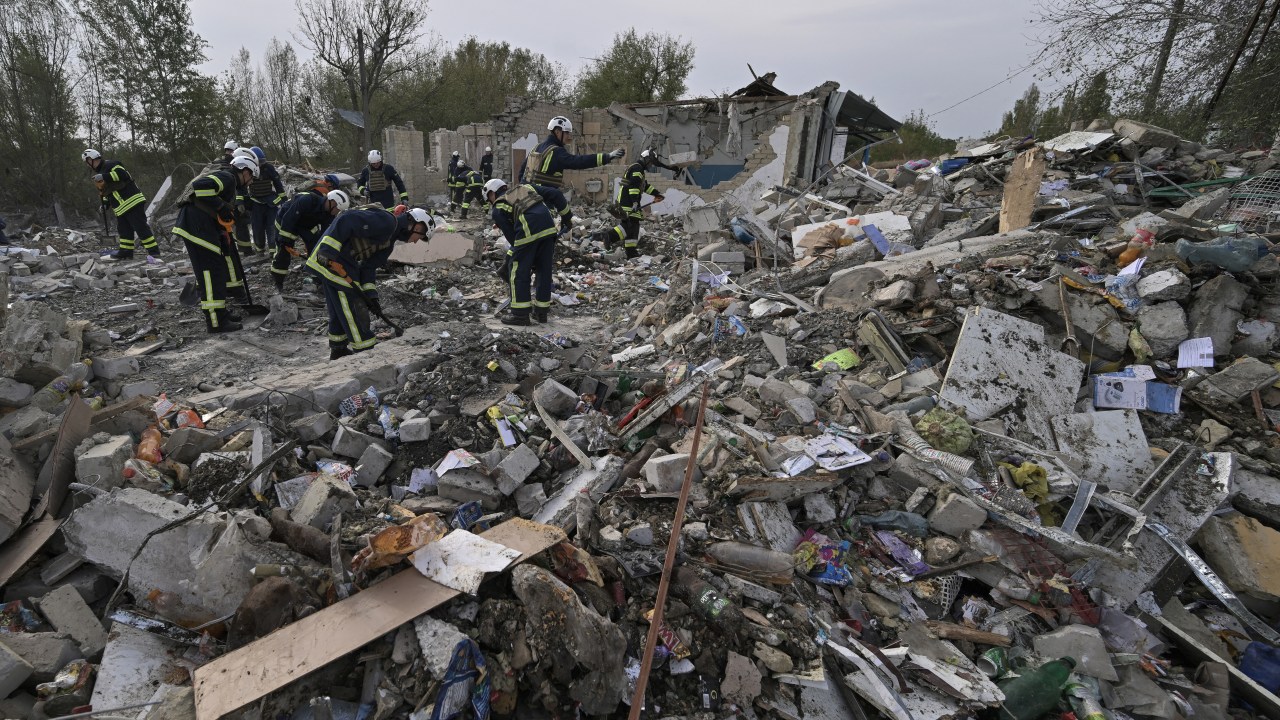 Ukrainian emergency personnel clear debris on the site of a Russian strike which hit a shop and cafe in the village of Groza, some 30 kilometres west of Kupiansk, on October 6, 2023, amid the Russian invasion of Ukraine. A Russian strike on October 5, 2023, killed at least 52 people gathered for a wake at a shop and cafe in an eastern Ukrainian village, officials said. Interior Minister Igor Klymenko said the victims had gathered to remember a deceased villager in Groza in the Kharkiv region which has a population of 330. (Photo by Genya SAVILOV / AFP)