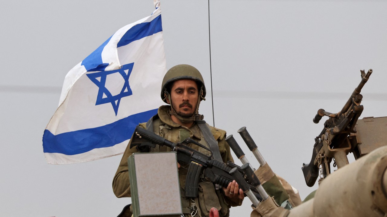An Israeli soldier rides on an armoured vehicle as the army takes positions in their armoured vehicles near the border with Gaza in southern Israel on October 9, 2023. Stunned by the unprecedented assault on its territory, a grieving Israel has counted over 700 dead and launched a withering barrage of strikes on Gaza that have raised the death toll there to 493 according to Palestinian officials. (Photo by JACK GUEZ / AFP)