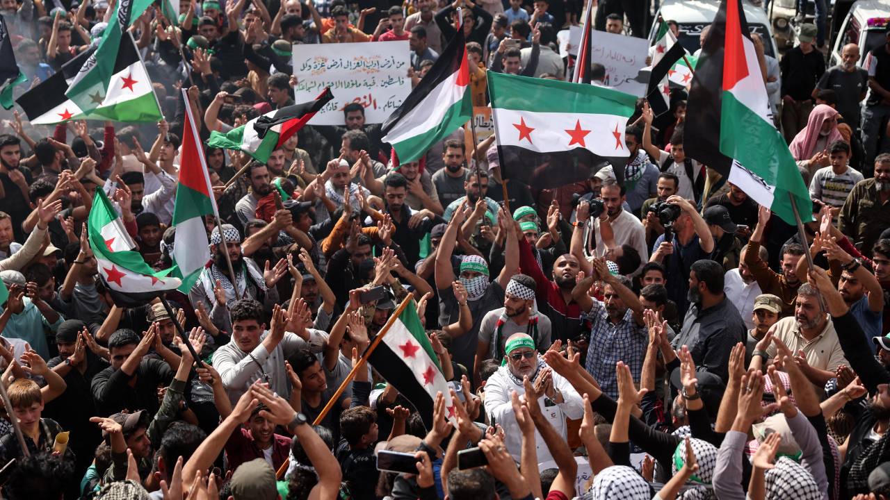 Protesters wave Palestinian and Syrian opposition flags as the rally in support of Palestinians in the Gaza Strip, in the rebel-held town of Atme in Syria's northwestern Idlib province on October 18, 2023. A blast ripped through a hospital in war-torn Gaza killing hundreds of people late on October 17, sparking global condemnation and angry protests around the Muslim world. Israel and Palestinians traded blame for the incident, which an "outraged and deeply saddened" US President Joe Biden denounced while en route to the Middle East. (Photo by OMAR HAJ KADOUR / AFP)