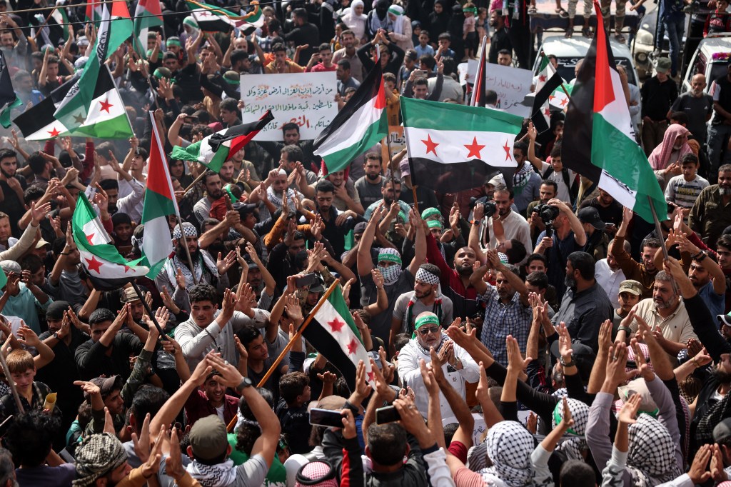 Protesters wave Palestinian and Syrian opposition flags as the rally in support of Palestinians in the Gaza Strip, in the rebel-held town of Atme in Syria's northwestern Idlib province on October 18, 2023. A blast ripped through a hospital in war-torn Gaza killing hundreds of people late on October 17, sparking global condemnation and angry protests around the Muslim world. Israel and Palestinians traded blame for the incident, which an "outraged and deeply saddened" US President Joe Biden denounced while en route to the Middle East. (Photo by OMAR HAJ KADOUR / AFP)