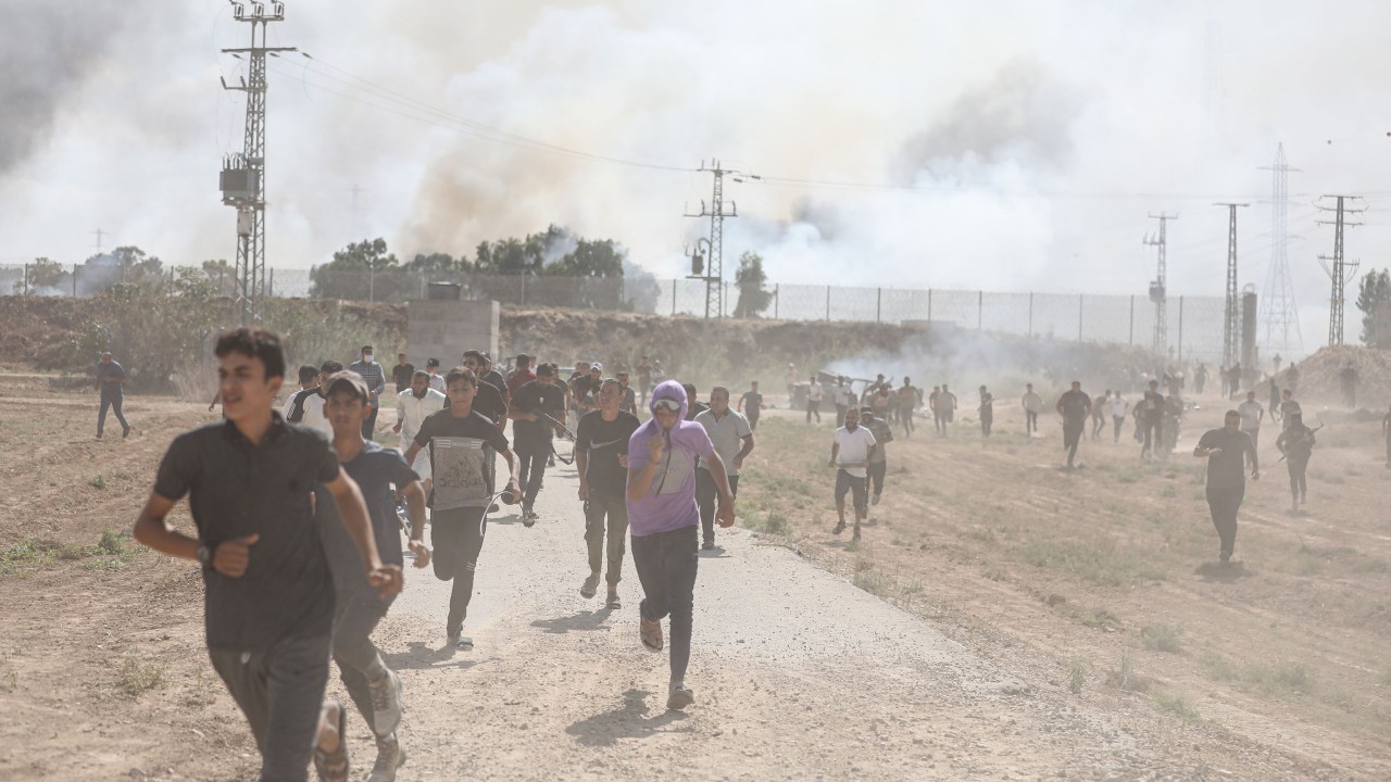 Pessoas correm diante de confrontos entre grupos palestinos e forças de defesa de Israel em Gaza (07/10/2023)