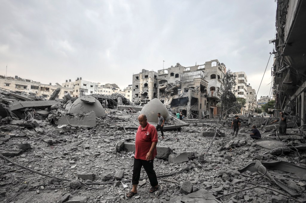 Palestinos caminham entre prédios destruídos na Faixa de Gaza após bombardeio das forças de Israel