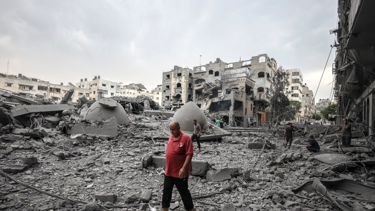 Palestinos caminham entre prédios destruídos na Faixa de Gaza após bombardeio das forças de Israel