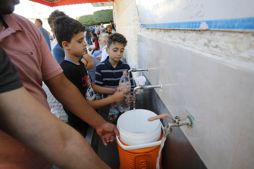 Palestinos enchem poucos baldes com água potável em meio à escassez no trecho, em Deir-Al Balah, Gaza. 15/10/2023
