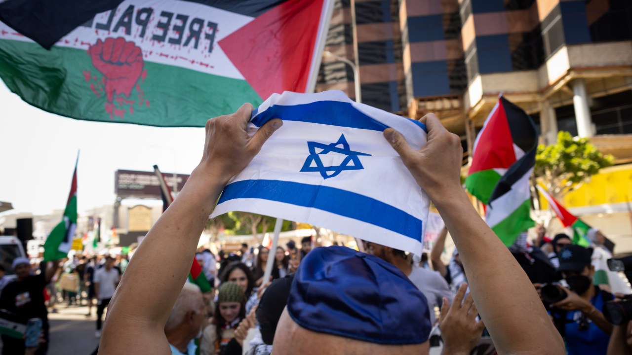 Um homem não identificado, usando um quipá, tenta segurar uma pequena bandeira israelense sobre sua cabeça, enquanto milhares de apoiadores pró-Palestina se reuniam em frente ao Consulado de Israel, em Los Angeles, nos EUA. 14/10/2023