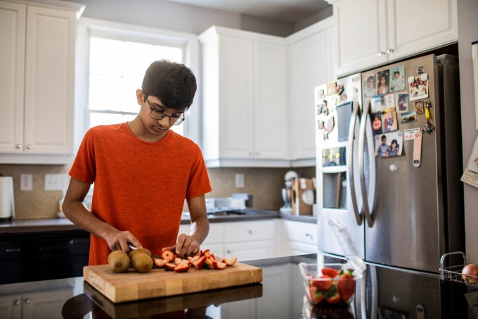 High school boy cutting fruit in kitchen