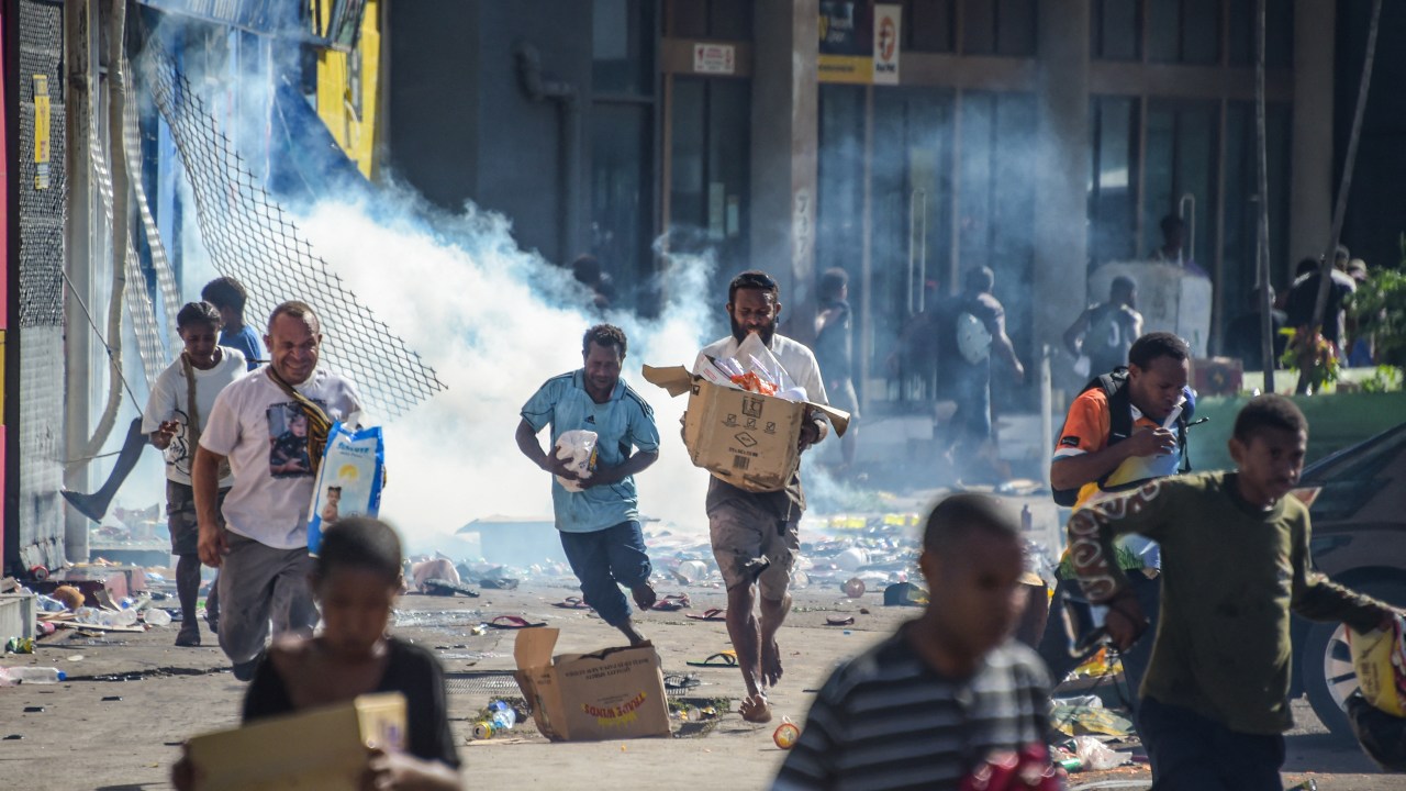 Pessoas correm com mercadorias enquanto multidões saqueiam joas em Port Moresby, na Papua-Nova Guiné. 10/01/2024