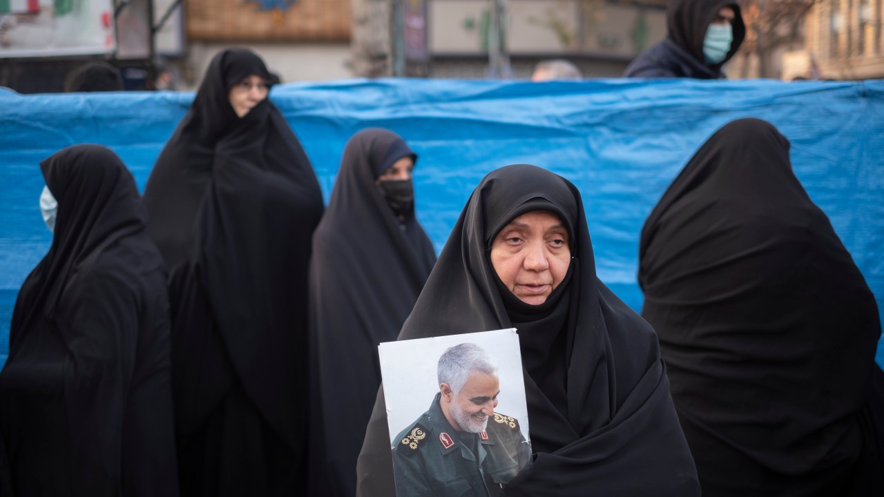 Mulheres iranianas comparecem a um funeral de mártires desconhecidos da guerra Irã-Iraque (1980-88) no centro de Teerã, enquanto uma delas segura um retrato do ex-comandante iraniano da Força Quds do Corpo da Guarda Revolucionária Islâmica (IRGC), major-general Qasem Soleimani