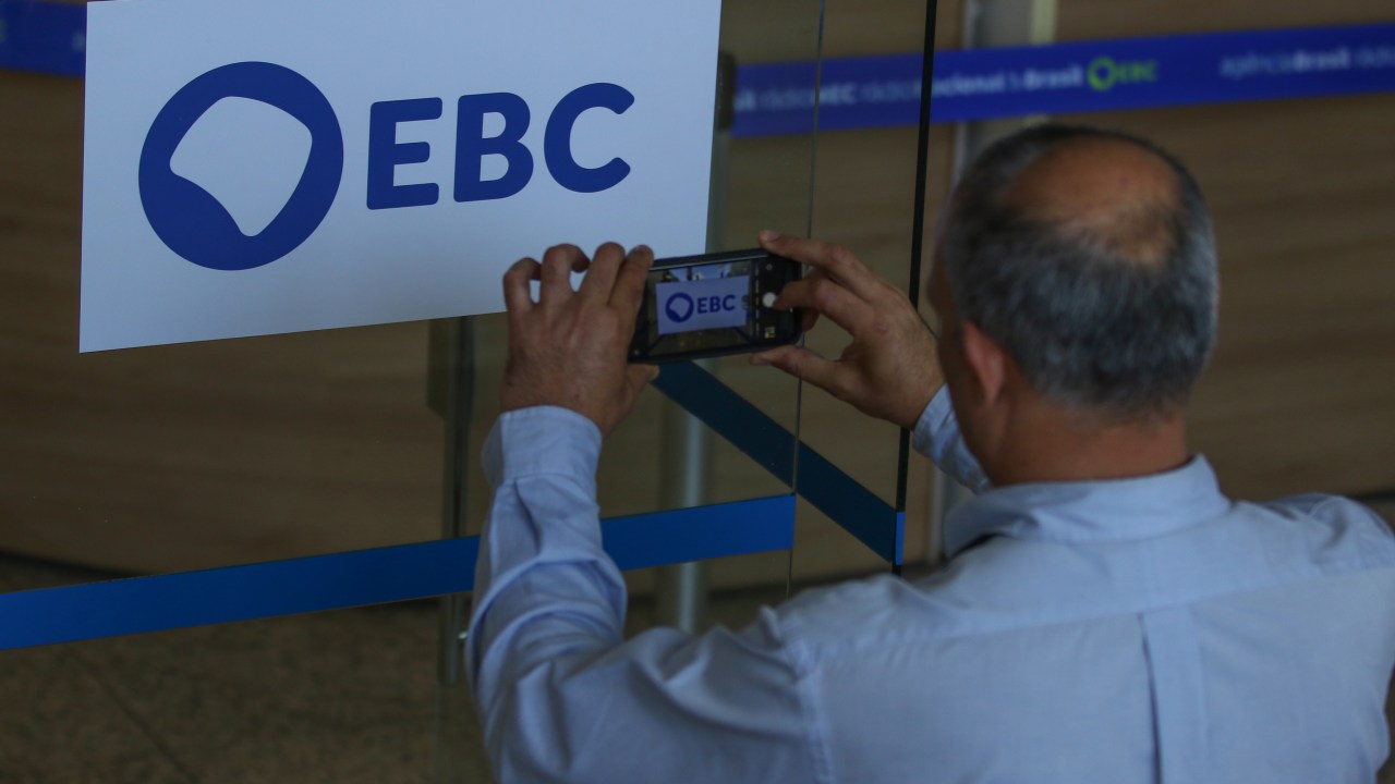 Homem fotografa a nova marca da Empresa Brasil de Comunicação (EBC), na entrada da empresa, em Brasília