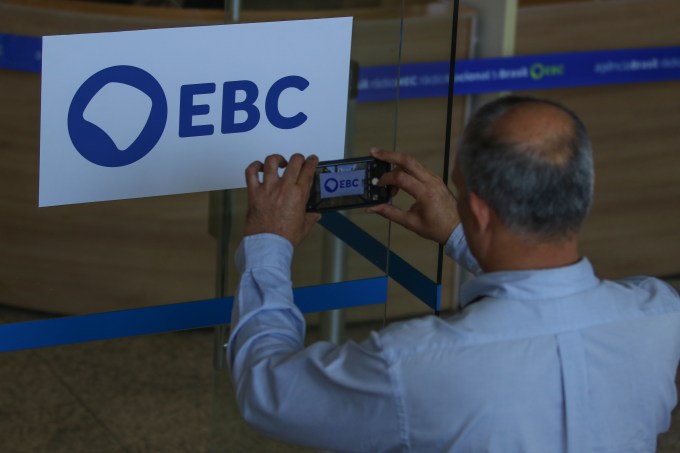 Homem fotografa a nova marca da Empresa Brasil de Comunicação (EBC), na entrada da empresa, em Brasília