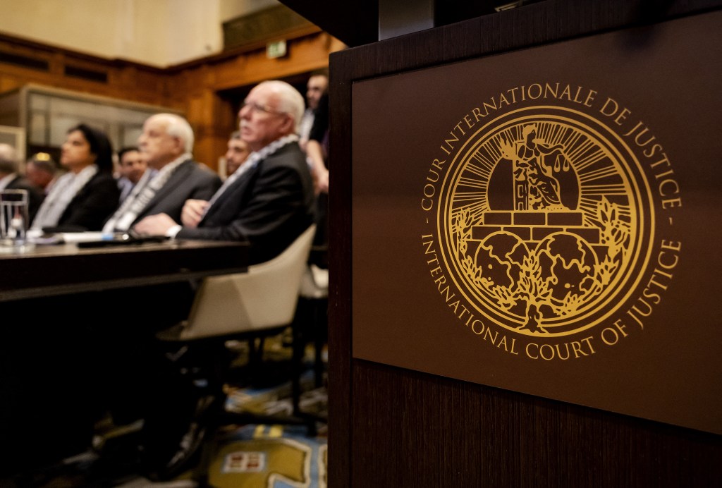 The Logo of the International Court of Justice (ICJ) is seen next to Minister of Foreign Affairs of the Palestinian Authority Riyad al-Maliki (R) and members of his delegation as they listen at the start of a hearing at the ICJ on the legal consequences of the Israeli occupation of Palestinian territories, in The Hague on February 19, 2024. (Photo by Robin van Lonkhuijsen / ANP / AFP) / Netherlands OUT