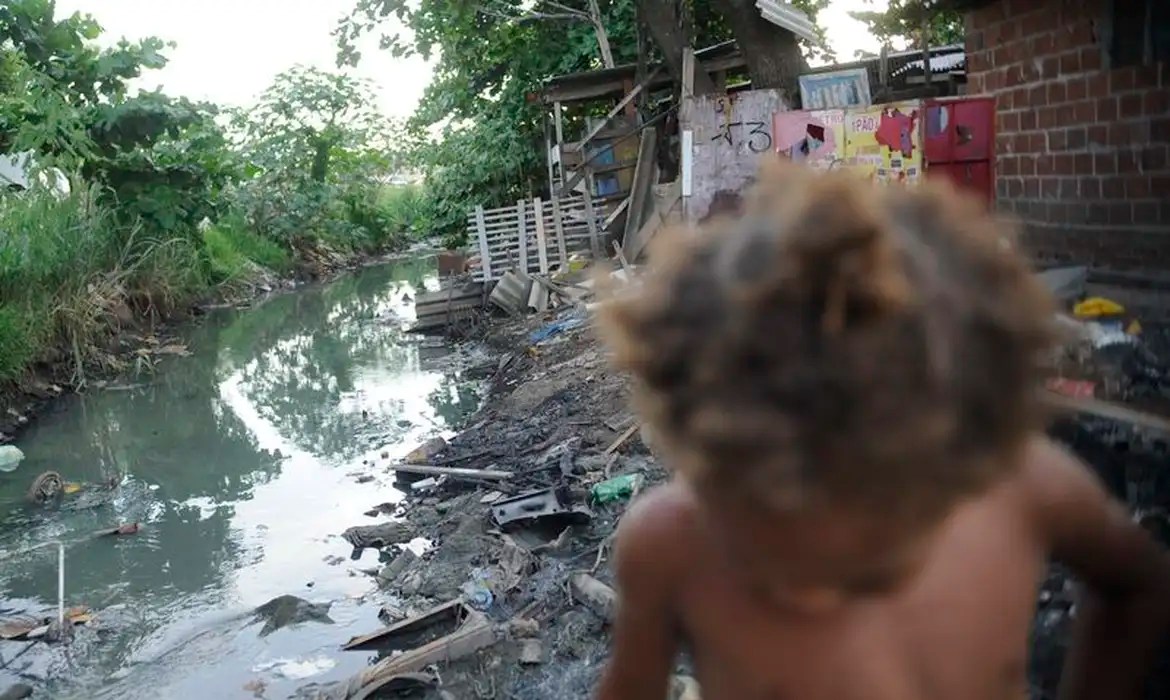 Criança caminha próximo ao esgoto, no Complexo da Maré, no Rio de Janeiro