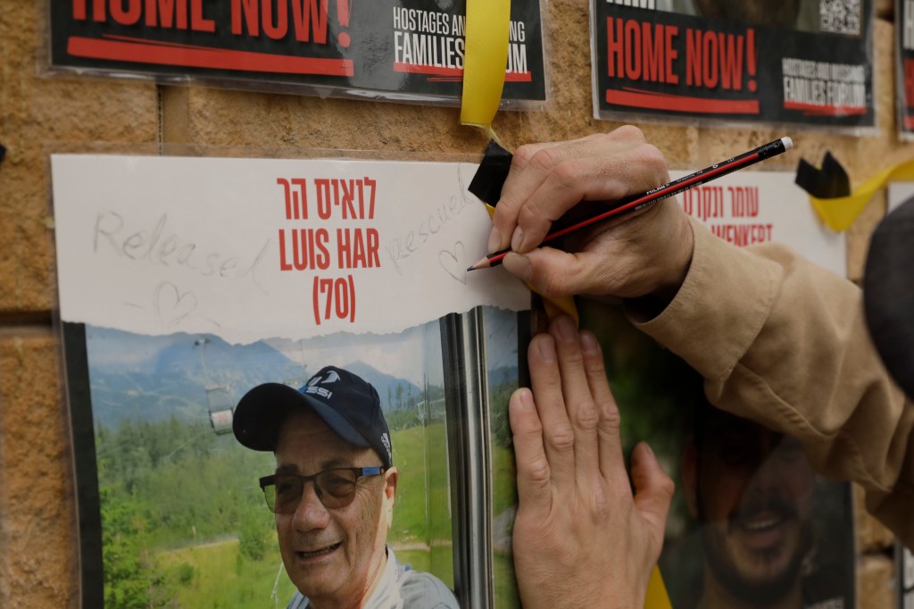 Um homem escreve "libertado" e "resgatado" em um cartaz do israelense desaparecido Luis Har em uma parede na Praça dos Reféns, em Tel Aviv, Israel.