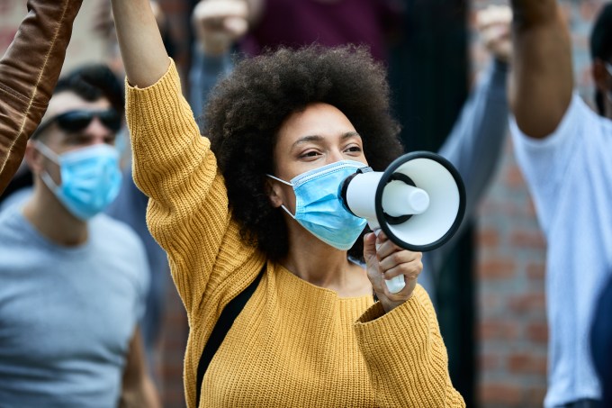 Black woman with protective face mask shouting through megaphone