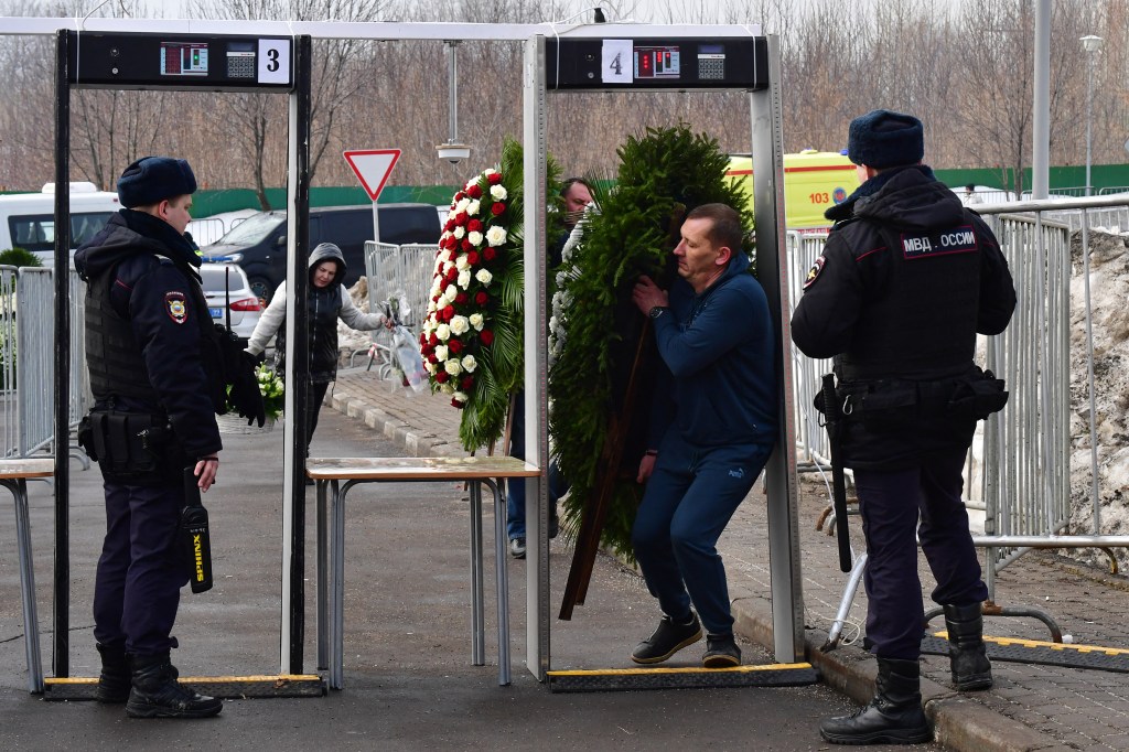 A man carrying a wreath passes through a metal detector security gate at the Borisovo cemetery ahead of the burial of late Russian opposition leader Alexei Navalny in Moscow's district of Maryino on March 1, 2024. (Photo by Olga MALTSEVA / AFP)
