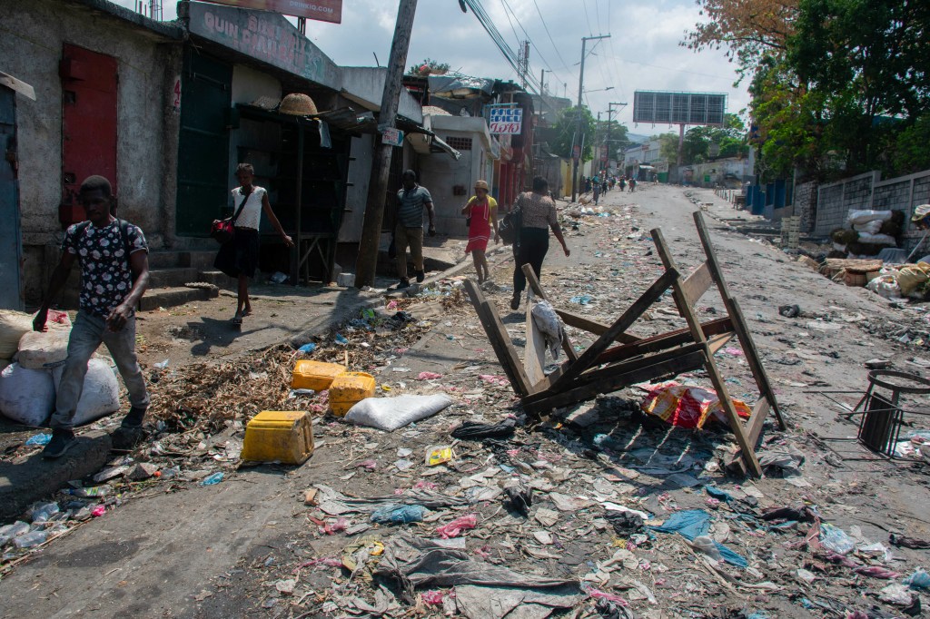 People walk past a barricade in a road in Port-au-Prince, Haiti, on March 20, 2024. Negotiations to form a transitional council to govern Haiti advanced on March 20, as the United States airlifted more citizens to safety from gang violence that has plunged the impoverished country into chaos. (Photo by Clarens SIFFROY / AFP)