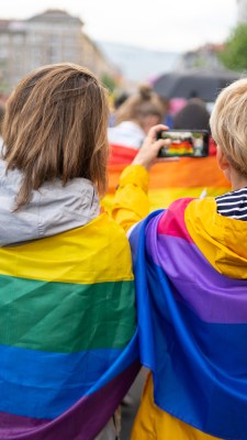 Duas mulheres enroladas em bandeiras LGBT seguram bandeiras do movimento Bi durante parada LGBT