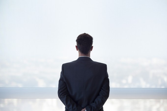 Businessman looking out high rise window at view of city below, rear view
