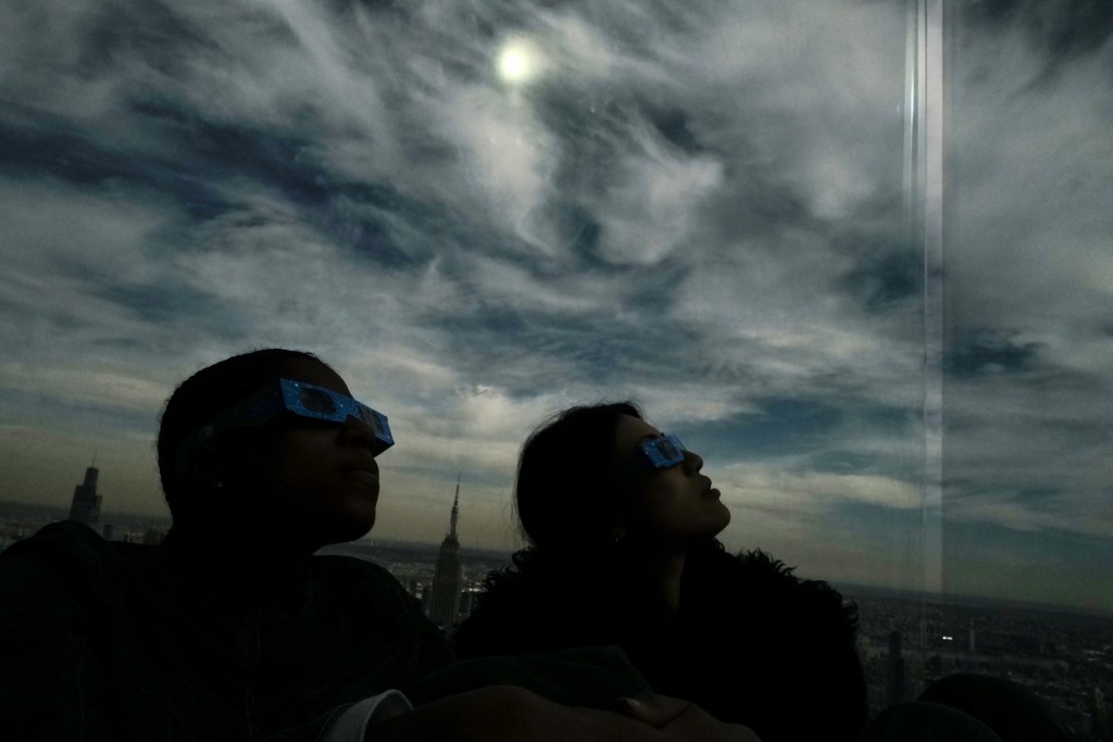 People look toward the sky at the 'Edge at Hudson Yards' observation deck during a total solar eclipse across North America, in New York City on April 8, 2024. This year's path of totality is 115 miles (185 kilometers) wide and home to nearly 32 million Americans, with an additional 150 million living less than 200 miles from the strip. The next total solar eclipse that can be seen from a large part of North America won't come around until 2044. (Photo by Charly TRIBALLEAU / AFP)