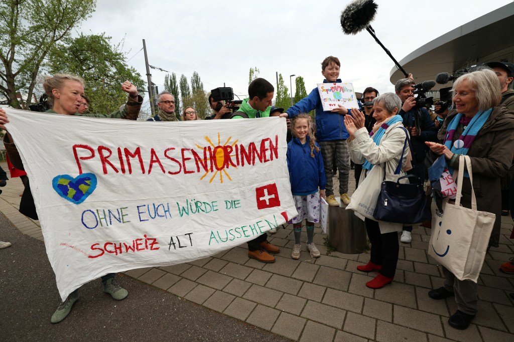 Manifestantes segurando um cartaz escrito "Sem você, a Suíça seria mais velha" antes da decisão do Tribunal Europeu dos Direitos Humanos (TEDH) sobre o caso movido pelo grupo de idosas suíças contra o governo do país em relação à falta de medidas de combate ao aquecimento global. 09/04/2024