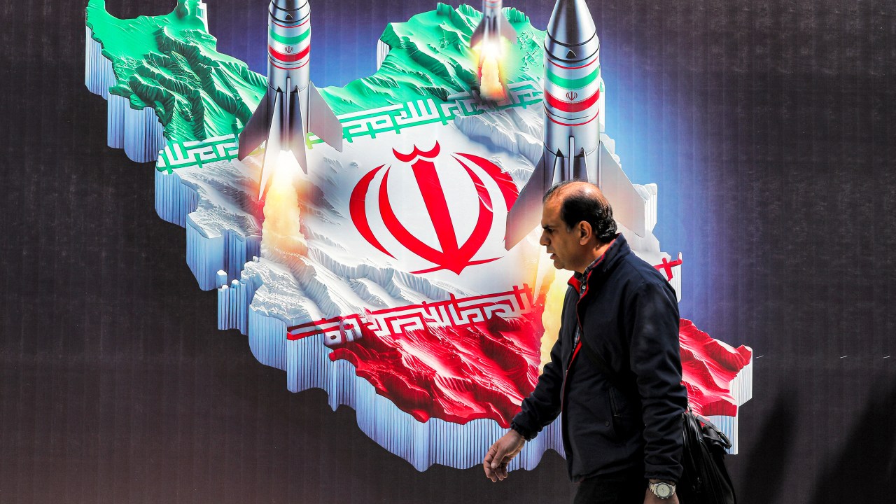 A man walks past a banner depicting missiles launching from a representation of the map of Iran coloured with the Iranian flag in central Tehran on April 15, 2024. Iran on April 14 urged Israel not to retaliate militarily to an unprecedented attack overnight, which Tehran presented as a justified response to a deadly strike on its consulate building in Damascus. (Photo by ATTA KENARE / AFP)