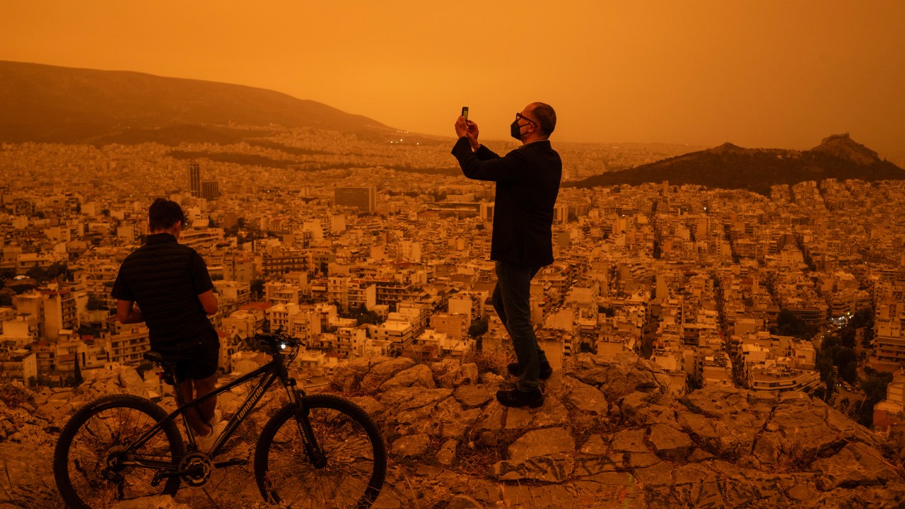 A man takes a photograph of the city of Athens from Tourkovounia hill, as southerly winds carry waves of Saharan dust to the city, in Athens, on April 23, 2024. Clouds of dust blown in from the Sahara covered Athens and other Greek cities on April 23, 2024, one of the worst such episodes to hit the country since 2018, officials said. The yellow-orange haze smothered several regions, limiting visibility and prompting warnings of breathing risks from the authorities. (Photo by Angelos TZORTZINIS / AFP)
