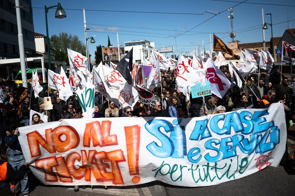 Manifestantes segurando um cartaz escrito "Não aos ingressos, sim às casas e serviços à todos" em protesto contra a cobrança da taxa para turistas em Veneza, Itália. 25/04/2024.