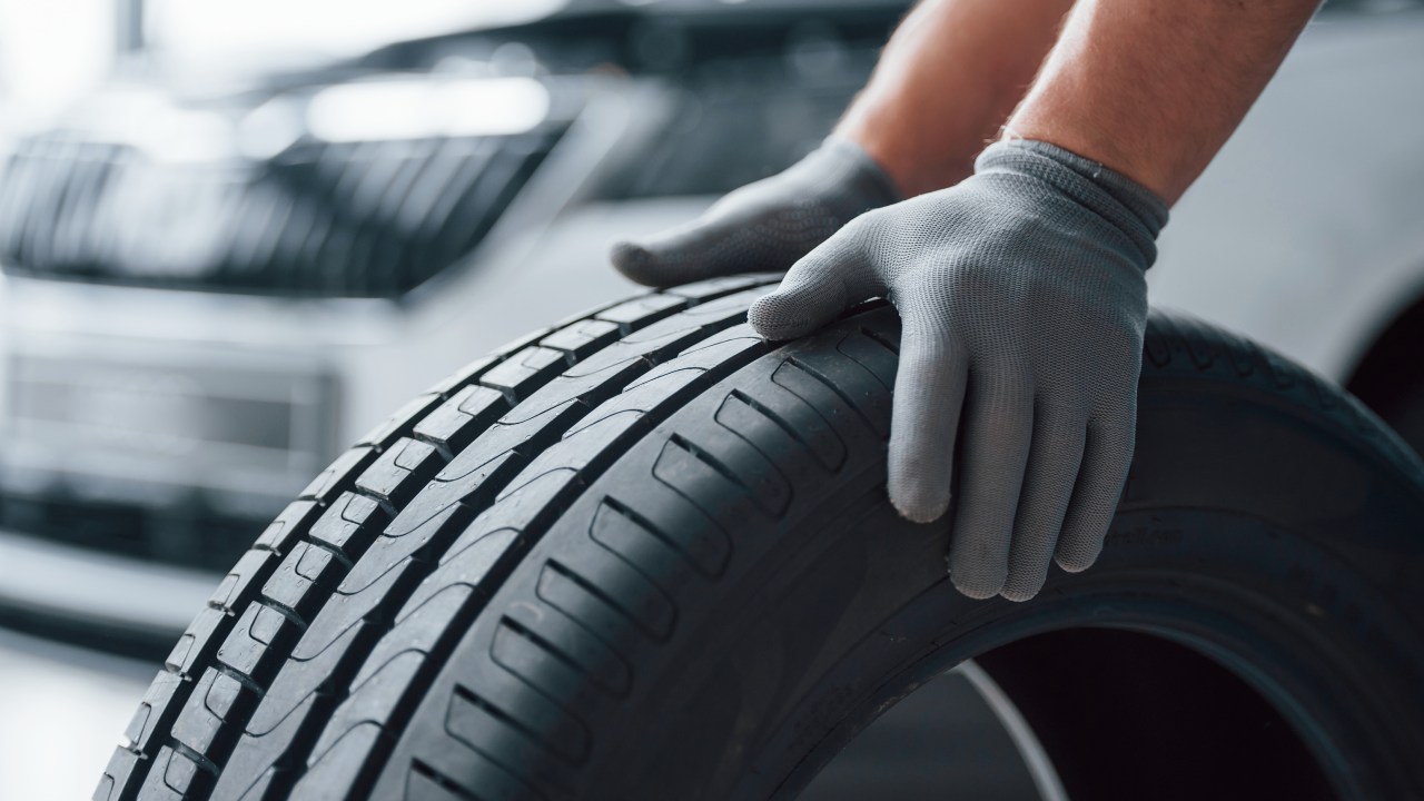 Hands only. Mechanic holding a tire at the repair garage. Replacement of winter and summer tires.