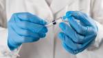 A doctor in a white coat and protective gloves holds a medicine in a syringe or a covid-19 Vaccine. The hand of the medical worker knocks on the syringe and knocks out the air with his finger. The concept of health care, vaccination, treatment of diseases