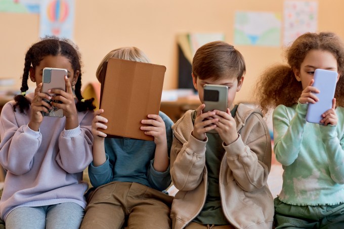 Group of young children holding smartphones and hiding faces