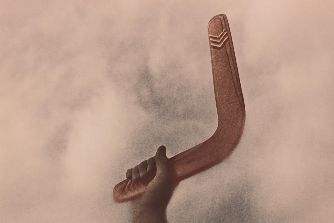 Hand holding boomerang against sky, close-up (tinted B&W)