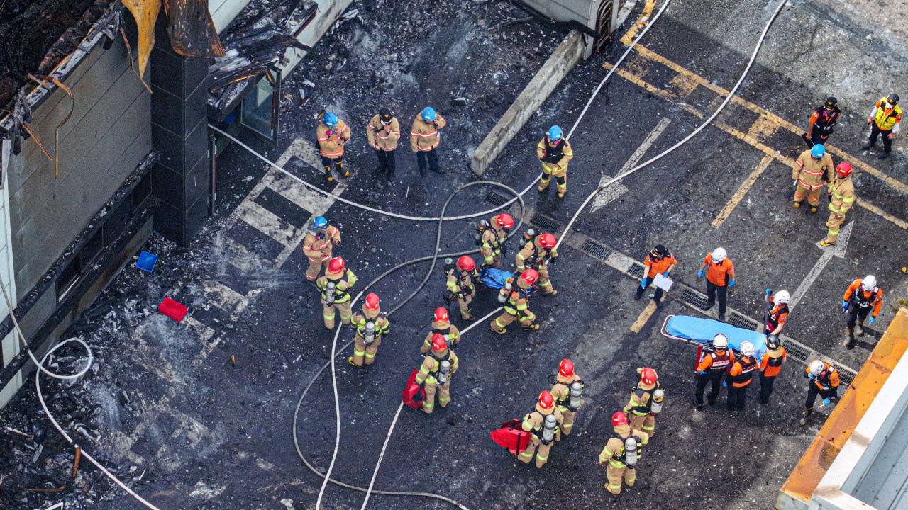 In an aerial view, firefighters carry a dead body after extinguishing a fire at a lithium battery factory in Hwaseong on June 24, 2024. Around 20 bodies have been found at a South Korean lithium battery factory after a massive blaze on June 24, the Yonhap news agency said, with firefighters saying they were still searching the building. (Photo by YONHAP / AFP) / - South Korea OUT / NO ARCHIVES - RESTRICTED TO SUBSCRIPTION USE