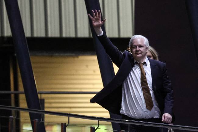 WikiLeaks founder Julian Assange waves after arriving at Canberra Airport in Canberra on June 26, 2024, after he pleaded guilty at a US court in Saipan to a single count of conspiracy to obtain and disseminate US national defence information. WikiLeaks founder Julian Assange returned home to Australia to start life as a free man June 26 after admitting he revealed US defence secrets in a deal that unlocked the door to his London prison cell. (Photo by David GRAY / AFP)