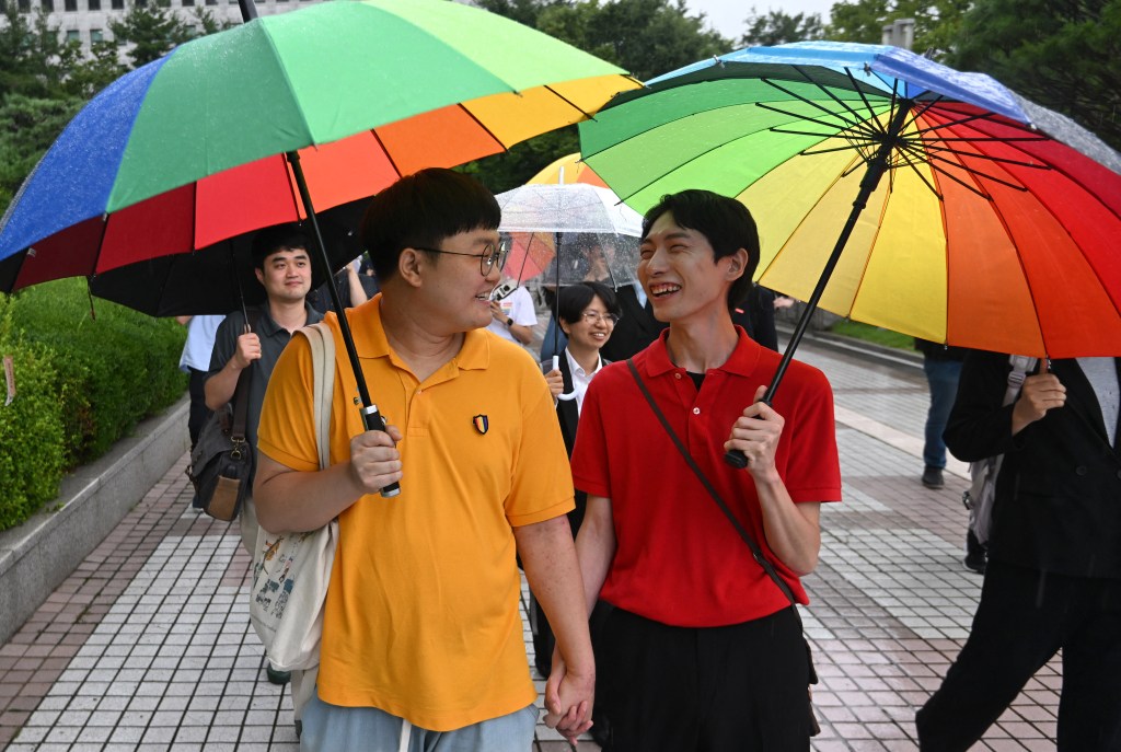 South Korean same-sex couple So Seong-wook (L) and Kim Yong-min (R) leave the Supreme Court building in Seoul on July 18, 2024 after the court's ruling on a lawsuit against the National Health Insurance Service for their dependent family status. South Korea's Supreme Court recognised new rights for same-sex couples on July 18, saying the state must provide health insurance for a gay man's partner in a landmark ruling that left activists weeping for joy. (Photo by Jung Yeon-je / AFP)