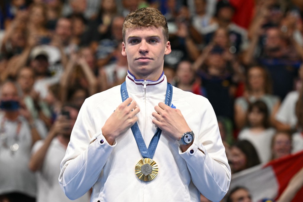 Gold medallist France's Leon Marchand stands on the podium of the men's 200m butterfly swimming event during the Paris 2024 Olympic Games at the Paris La Defense Arena in Nanterre, west of Paris, on July 31, 2024. (Photo by Jonathan NACKSTRAND / AFP)