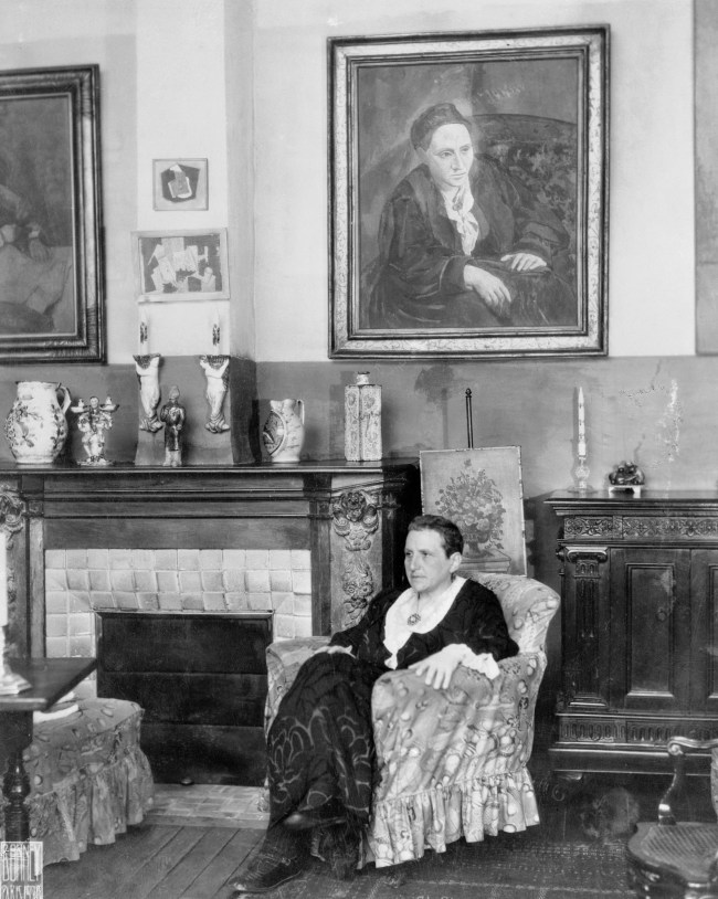 (Original Caption) Paris, France: Writer Gertrude Stein seated before a portrait of herself that was painted by Picasso.