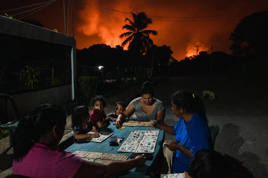 Céus Vermelhos, Águas Verdes: Vizinhos jogam Animal Lotto sob um céu iluminado por uma dasmaiores chamas de gás do mundo. Punta de Mata, Venezuela, 5 de novembro de 2022