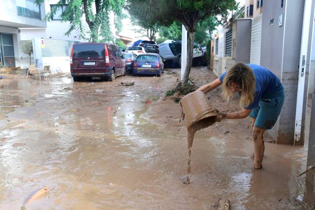 SPAIN-FLOODS A resident cleans her house next to cars piles due to mudslide in a flooded area in Picanya, near Valencia, eastern Spain, on October 30, 2024. Floods triggered by torrential rains in Spain's eastern Valencia region has left 51 people dead, rescue services said on October 30. (Photo by Jose Jordan / AFP)