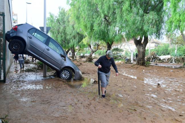 SPAIN-FLOODS A resident walks next to a car lifted up in a street covered in mud in a flooded area in Picanya, near Valencia, eastern Spain, on October 30, 2024. Floods triggered by torrential rains in Spain's eastern Valencia region has left 51 people dead, rescue services said on October 30. (Photo by Jose Jordan / AFP)