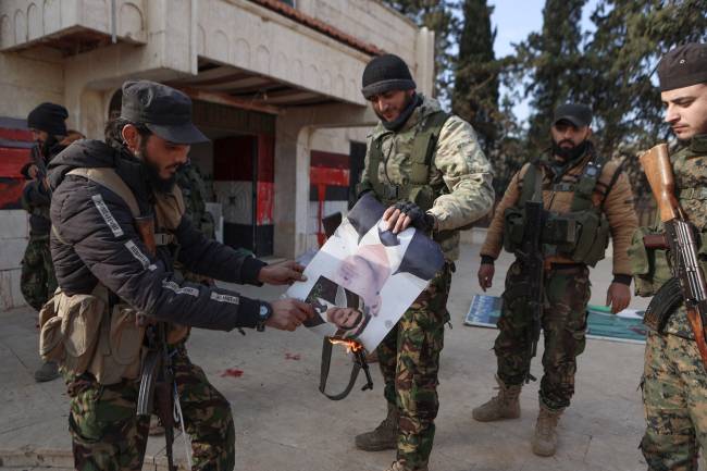 Fighters set alight a picture of Syrian President Bashar al-Assad in front of a building that was seized by jihadists in the area of Zarbah on November 29, 2024, as Hayat Tahrir al-Sham (HTS) jihadists and allied groups continue their offensive in Syria's northern Aleppo province against government forces. The jihadists along with Turkey-backed factions launched this week a shock offensive against Syrian regime troops and sparked the deadliest battle the country has seen in years, with the violence killing so far 242 people, according to the Syrian Observatory for Human Rights. The war monitor said most of the victims were combatants on both sides but also including civilians. (Photo by AAREF WATAD / AFP)