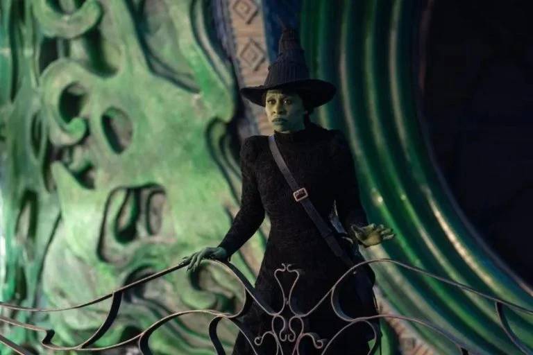 Elphaba, de Cynthia Erivo: silhueta sóbria e padrão texturizado para vestidos de cintura marcada e chapéu símbolo da bruxa